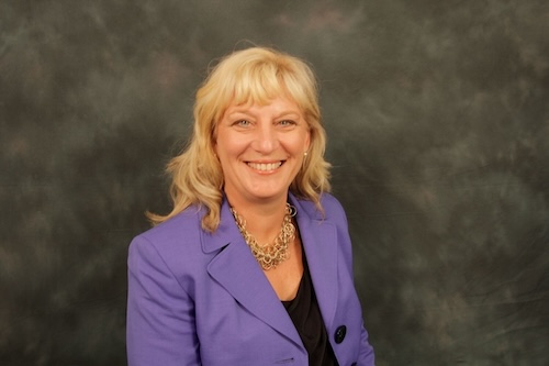 Headshot of a woman in a purple blazer smiling in front of a neutral backdrop