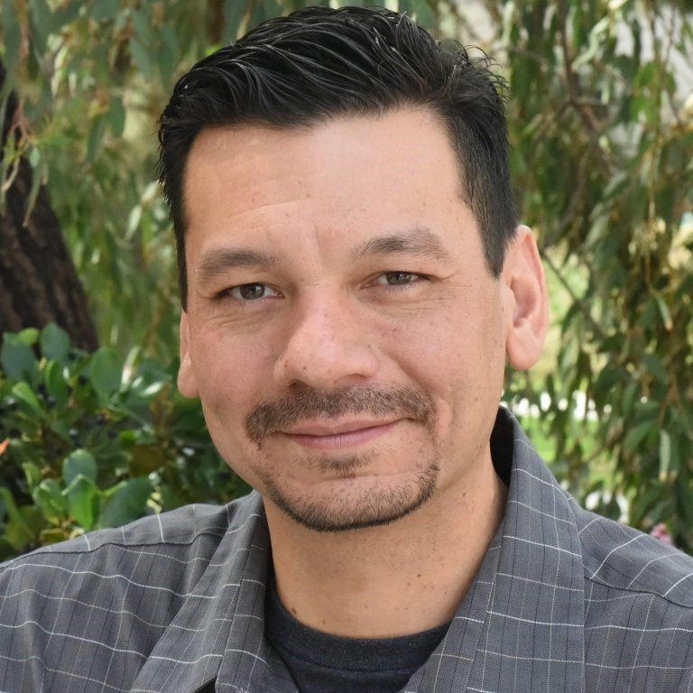 headshot of a man against green forest