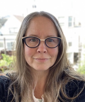photo of a woman with long hair and dark rimmed glasses smiling at the camera 