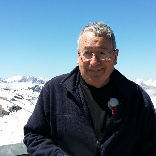 man in a black winter coat smiling for the camera in front of snow covered mountains