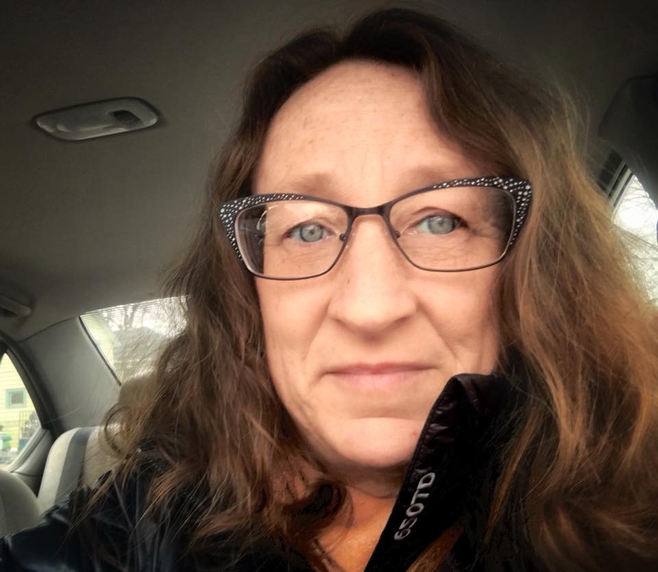 selfie of a woman in a black coat and jacket smiling at the camera while in a car