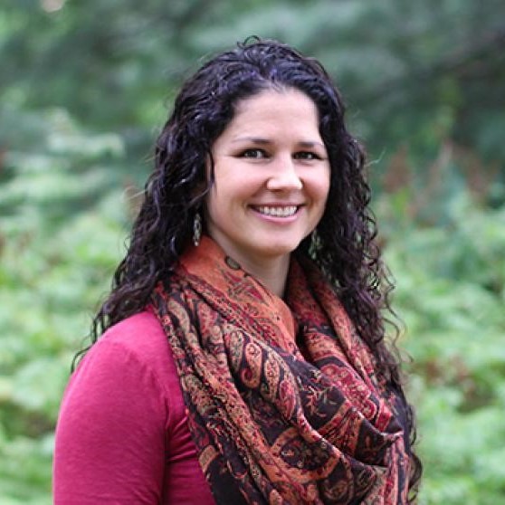 woman in a fuschia shirt, infinity scarf, smiling for the camera in front of greenery