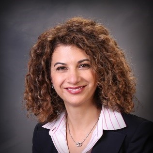 professional photo of a woman in a black sweater and white shirt smiling at the camera in front of a gray backdrop